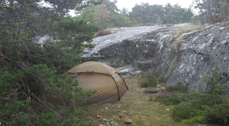 Bild. Tält uppslaget i skydd av en klippa. Det ser vått ut.