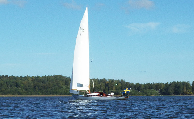 Bild. Segelbåt med spända segel och svensk flagga i aktern.