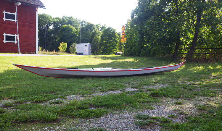 Bild. Arnes Acuta ligger på gräsmattan framför kanothuset.